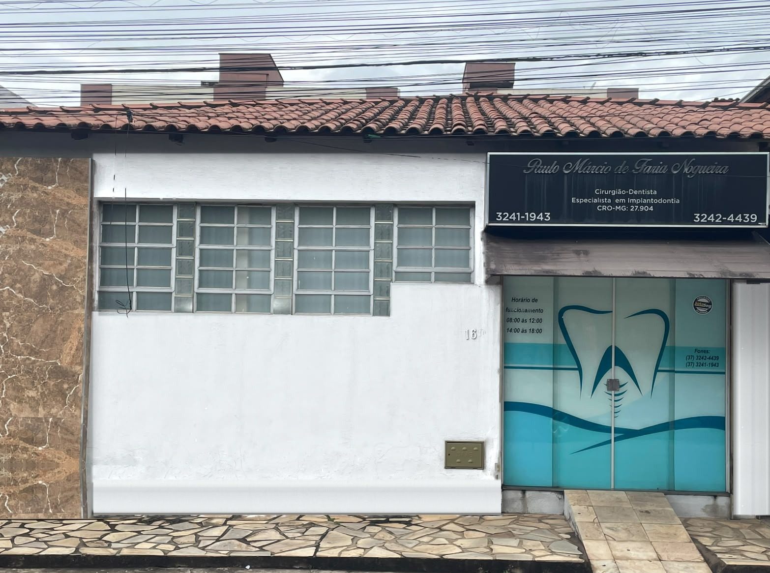 Fachada do consultório na Rua Marechal Deodoro, 169: parede branca com janelas, placa preta com o nome do Dr. Paulo Márcio e porta de vidro azul com o desenho de um dente